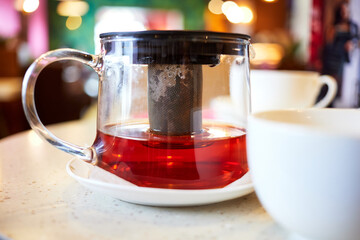 transparent teapot of black tea and cups on the table in the cafe.