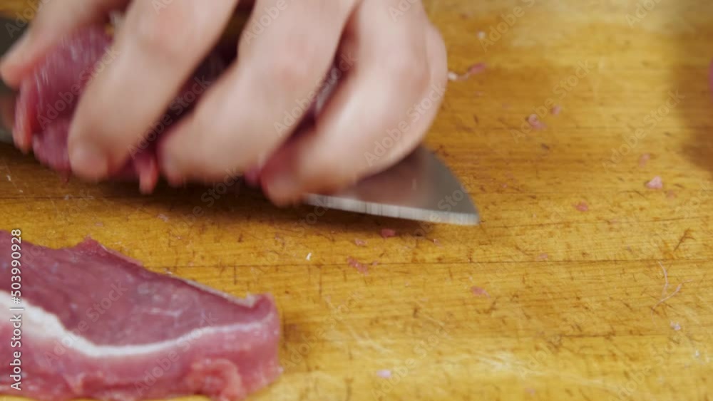 Wall mural Close-up of a cook slicing red meat on a kitchen board. He removes the sliced meat from the board. Top view. Cutting fresh meat in a home kitchen