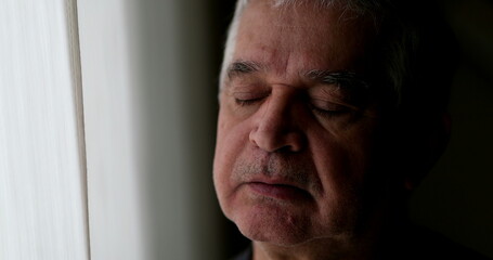 Contemplative older man standing by window thinking. Thoughtful sad depressed senior person