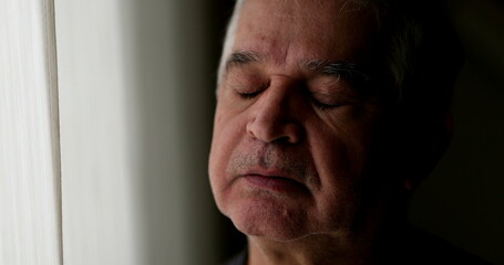 Contemplative older man standing by window thinking. Thoughtful sad depressed senior person