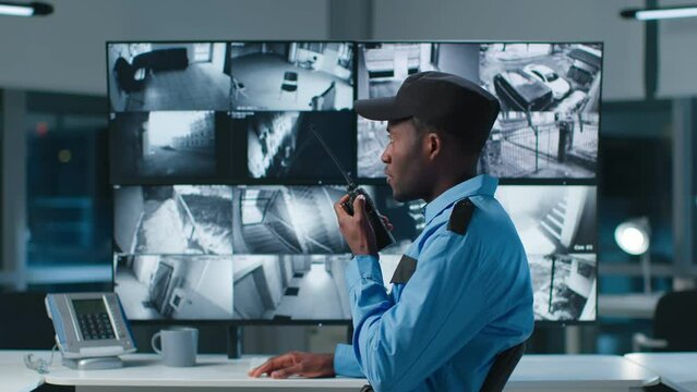 African-American security officer watching the screens talking on radio in control room 