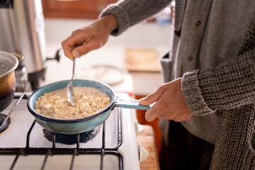 Unrecognizable young man is preparing soaked oats for breakfast using a gas stove - obrazy, fototapety, plakaty