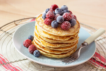 Stack of Pancakes Topped with Powdered Sugar and Frozen Raspberries and Blueberries on a Plate