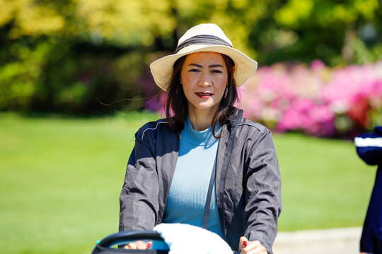 Une belle maman asiatique avec chapeau pousse une poussette dans un parc