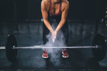 Unrecognizable muscular woman clapping hands with talc preparing for weightlifting with barbell at...