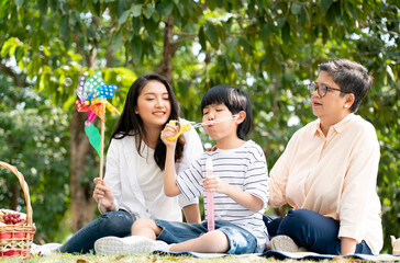 Asian family enjoys a picnic in the garden during their vacation. Grandma, mother and son relax in summer activities. living together and well-being. Concept mother's day