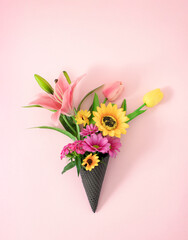 A Valentine or Wedding bouquet of fresh Spring pink and yellow flowers in cone ice cream. Creative pastel colored concept.