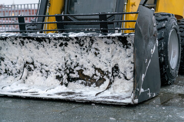 Snow plow tractor with a bucket in the snow remnants in the parking lot. Close up.
