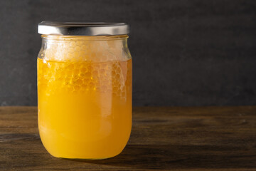 Jar of honey with honeycombs. Yellow transparent bee product. Half liter packaging with space for a label. Wooden background. Bee honey in a glass jar. Natural healthy food. Copy space.