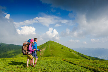 Young couple with backpacks hiking in the mountains and enjoying valley view