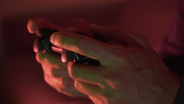 Close-up of a man's hands using joystick playing video games in a dark room with reddish tones