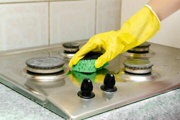 Cleaning dirty gas stove from grease, food leftovers deposits. woman's hand in protective glove...