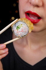 Light-skinned European-looking girl with red lips eats sushi rolls holding them in her hands with bamboo sticks