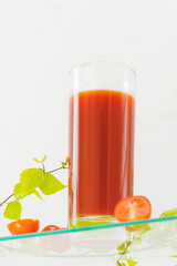 Glass of natural tomato juice with fresh cherry tomatoes and green branch on a glass shelves ona a white background. Healthy season food. Organic vegetable juce. Soft focus style. low angle view