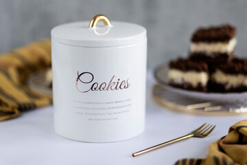 White ceramic cookie jar on grey background with cookies in the background. Healthy cookies, stylist cookie jar. 