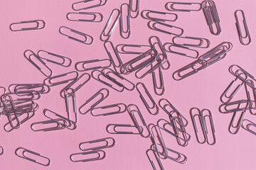 There are many paper clips on a pink background. Office background. Stationery. Layout. View from above.