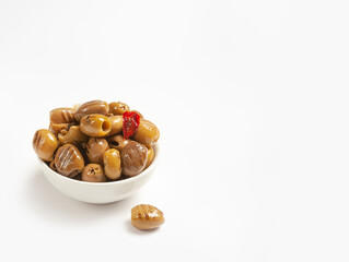 grilled green olives in oil, pitted, with red hot pepper and garlic in a white bowl on a light background side view, close-up, one olive on the table, copyspace