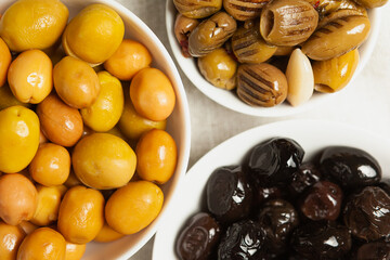 a set of three types of olives in white bowls - whole large green olives, black olives, green olives grilled in oil, pitted, top view, close-up, fragment