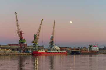 Obraz premium Three cranes in the port against clear evening sky. Moon shining in the sky