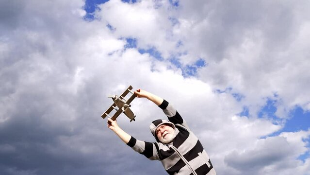 Happy elderly man pretend flying on model aircraft in sky, traveling