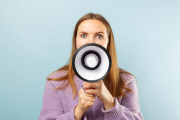 Obraz premium Young brunette woman shouting loudly while holding a megaphone on blue background. Concept of speech and announce, idea for marketing or sales