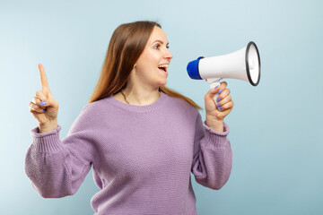 Young brunette woman shouting loudly while holding a megaphone on blue background. Concept of speech and announce, idea for marketing or sales