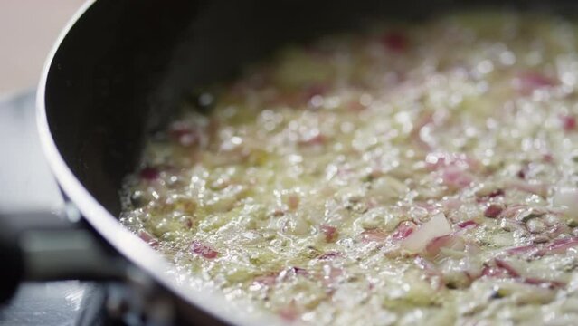 Close up tracking shot of chopped red onion and garlic being fried in sizzling butter in pan