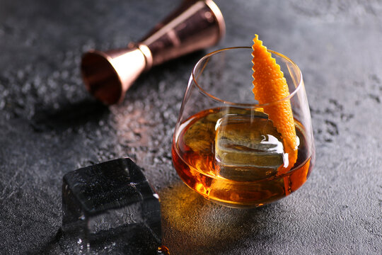 Drinks and beverages. Strong alcohol, whiskey, cognac, brandy on the rocks, orange twist in a glass on the black table. Restaurant, bar. Background image, copy space