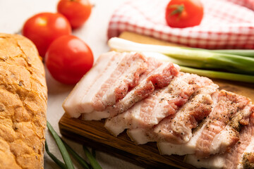 Board with pork fat, green onions, homemade bread and cherry tomatoes on a gray stone background. Salo. Delicious salty lard with pepper. Space for copy. Space for text.