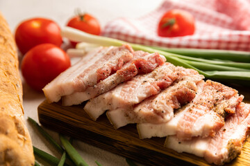Board with pork fat, green onions, homemade bread and cherry tomatoes on a gray stone background. Salo. Delicious salty lard with pepper. Space for copy. Space for text.