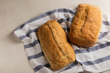 Fresh homemade bread on a kitchen towel on a gray cement background. Bread with flax seeds, sunflower seeds and sourdough bran. Organic homemade baked goods. Place to copy.
