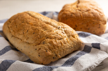 Fresh homemade bread on a kitchen towel on a gray cement background. Bread with flax seeds, sunflower seeds and sourdough bran. Organic homemade baked goods. Place to copy.