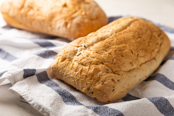 Fresh homemade bread on a kitchen towel on a gray cement background. Bread with flax seeds, sunflower seeds and sourdough bran. Organic homemade baked goods. Place to copy.
