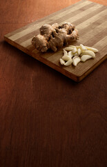 Ginger roots and garlic in a wooden cutting board. wooden background