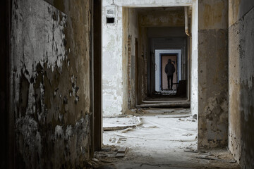 Fototapeta na wymiar Man stands in abandoned corridor. Rear view of man standing in corridor at abandoned building