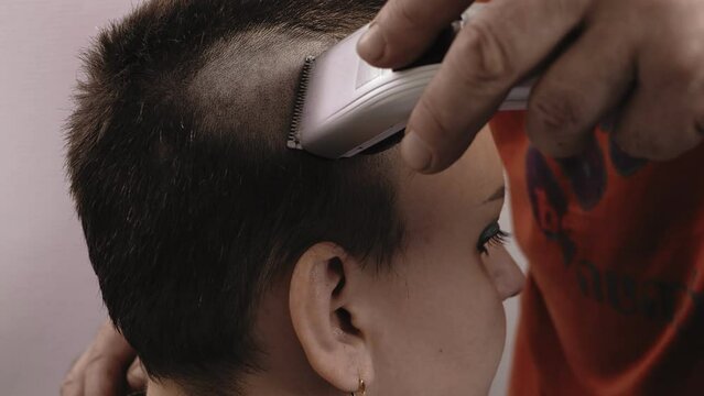 A man barber shaves a woman with a machine leaving a mohawk. Close-up