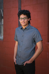 Obraz premium A young man stands in front of a red brick wall with his hands in his pockets.