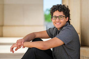 a curly-haired young man sits and leans against a stone pillar