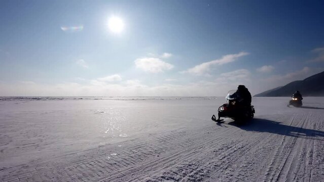 people are riding snowmobiles on frozen river or lake in sunny winter day, entertainment in winter