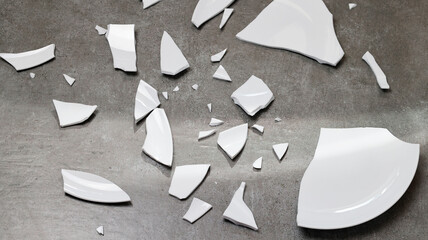 Closeup of broken dishes and white shards on the gray floor tiles background, splinters of break...