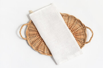 Flatlay composition with natural linen kitchen tea towel or napkin on wicker tray on white...