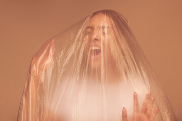 Emotional young woman screaming inside of plastic bag while feeling desperation, trap or pollution concept