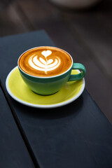 green mug of cappuccino with latte art on wooden background.