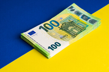 Stack of one hundred euro banknotes on Ukrainian flag. Money help from Europe to Ukraine concept