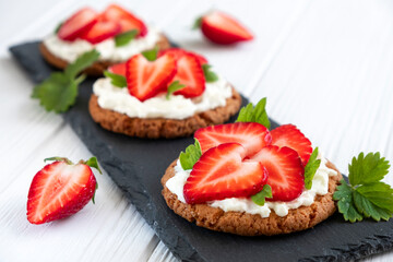Healthy crispbread bruschetta with strawberry and cream cheese on slate board. Healthy snack, clean eating or dieting concept. Recipe of vegan food for everyday cooking.