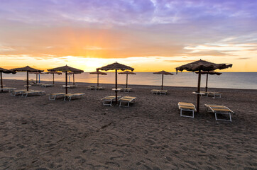  empty beach during beautiful sunrise or sunset with chaise loungues and nice umbrellas with blue sea