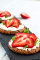 Strawberry bruschetta on rye bread with cottage cheese and mint. Healthy snack, keto diet or dieting concept. Recipe of vegan food for everyday cooking.