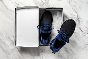 Pair of new mesh textile sneakers in the open box on a marble floor. Black blue fabric sneakers with laced fastening for active lifestyle and fitness. Buying shoes concept.
