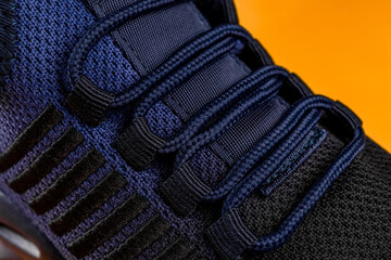 Laced up fastening of new sport shoe against orange background. Lacing of black blue mesh fabric...