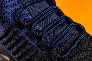 Laced up fastening of new sport shoe against orange background. Lacing of black blue mesh fabric sneakers macro. Modern textile sneakers with elastic laces for active lifestyle, sports and fitness.